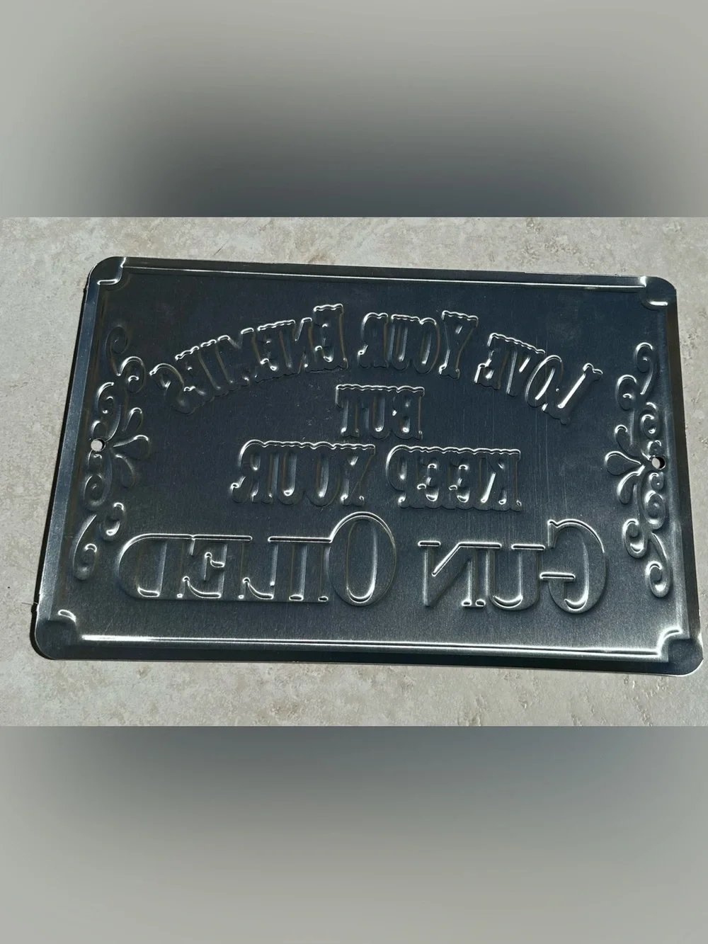 Aluminum sign “Love your enemies but keep your gun oiled”.
